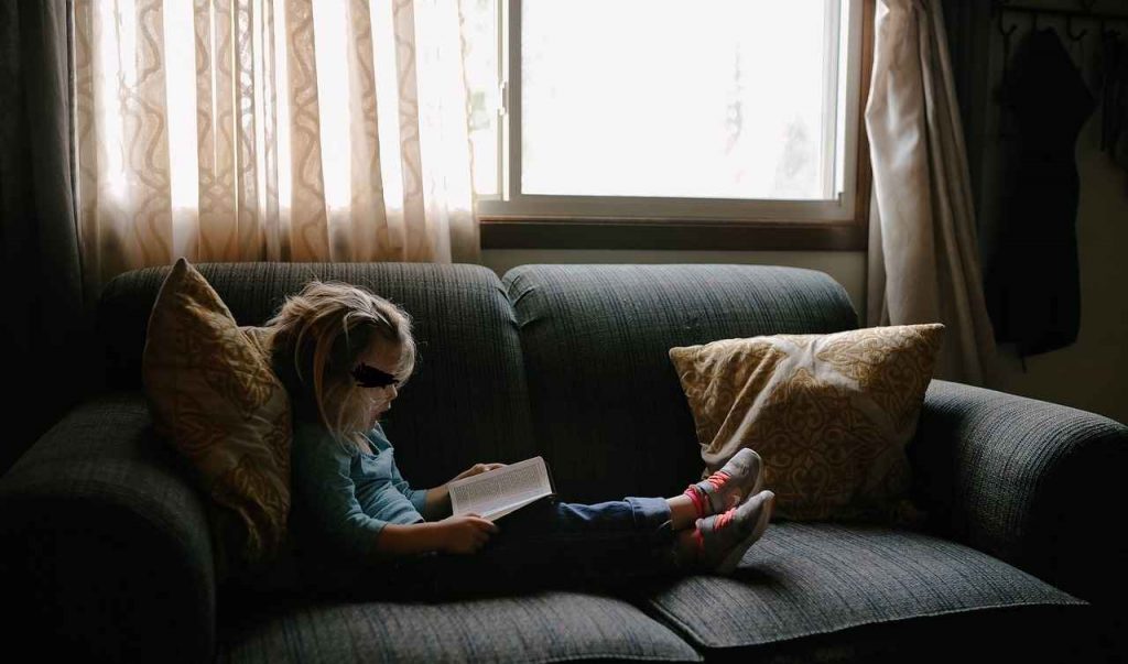 Bambina che legge seduta sul divano