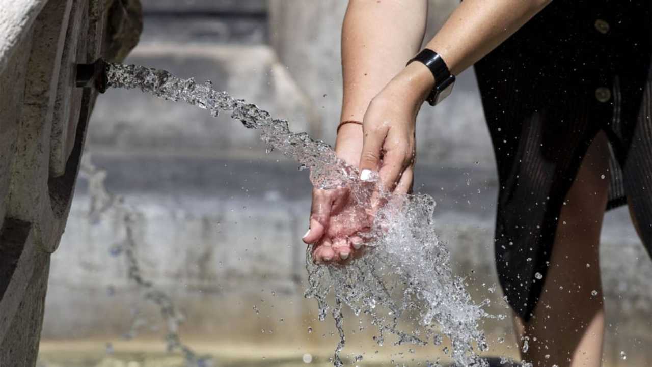 una ragazza si refrigera dal caldo in una fontanella