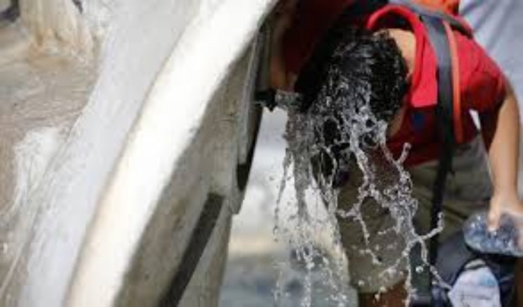 ragazzo si rinfresca sotto i getti di acqua di una fontana