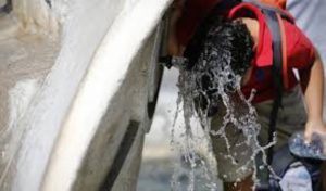 ragazzo si rinfresca sotto i getti di acqua di una fontana