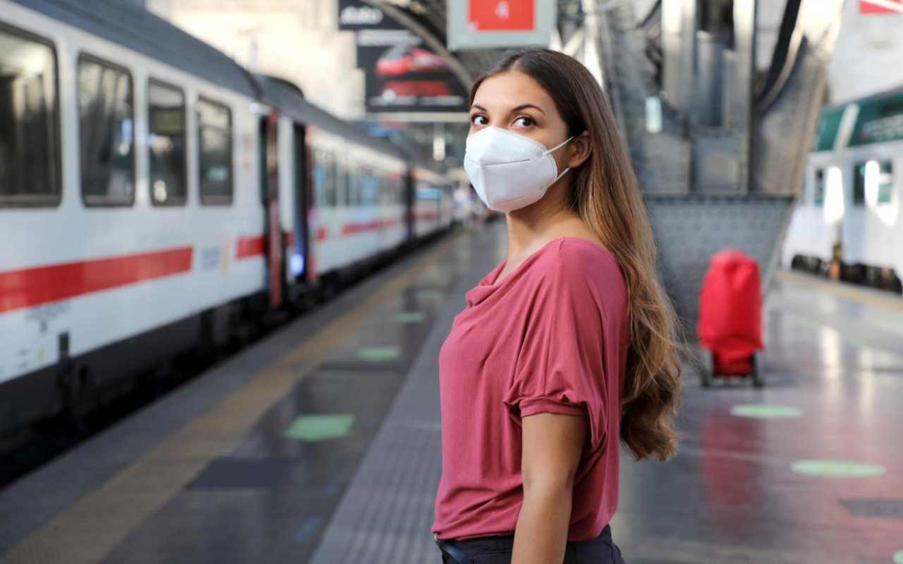 una ragazza indossa una mascherina con allo sfondo un treno