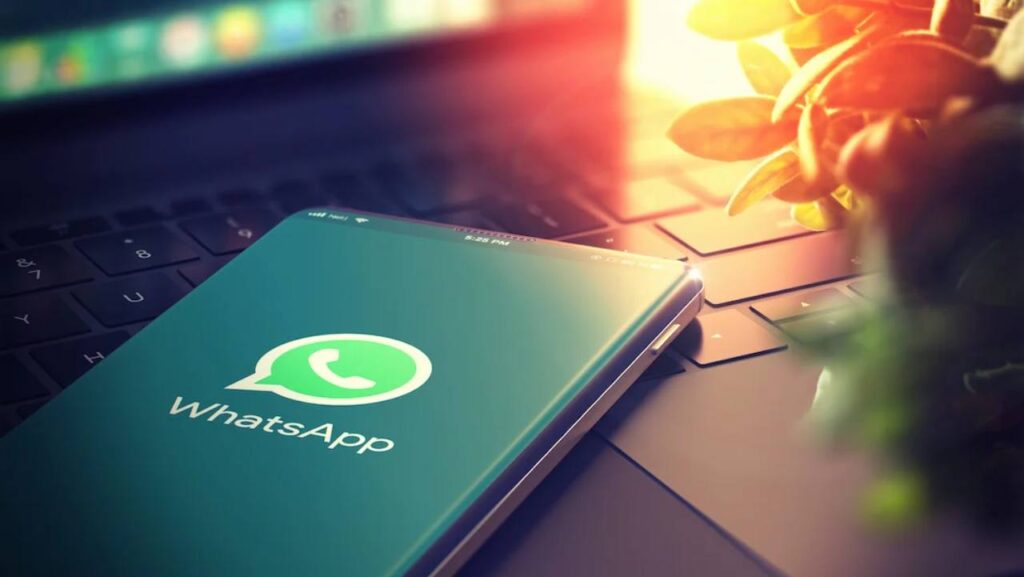 WhatsApp su schermo smartphone e luce del sole sullo sfondo con computer