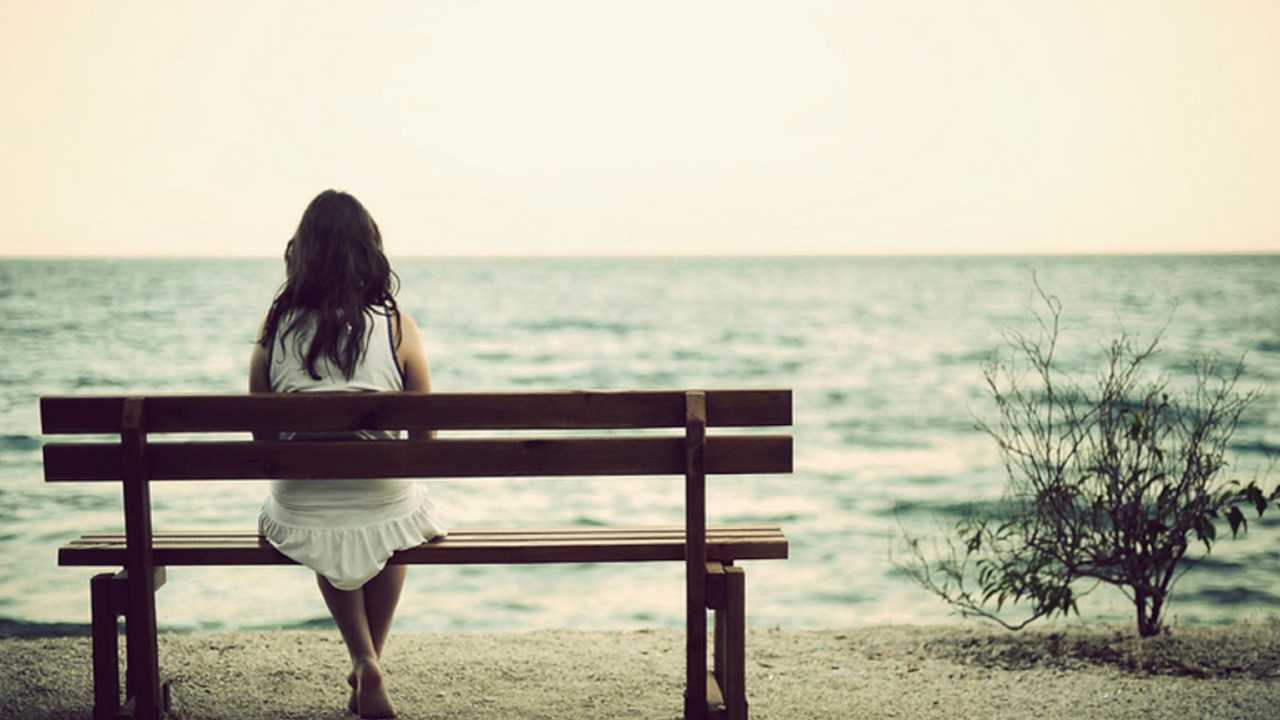 Una donna seduta di spalle su una panchina che guarda il mare