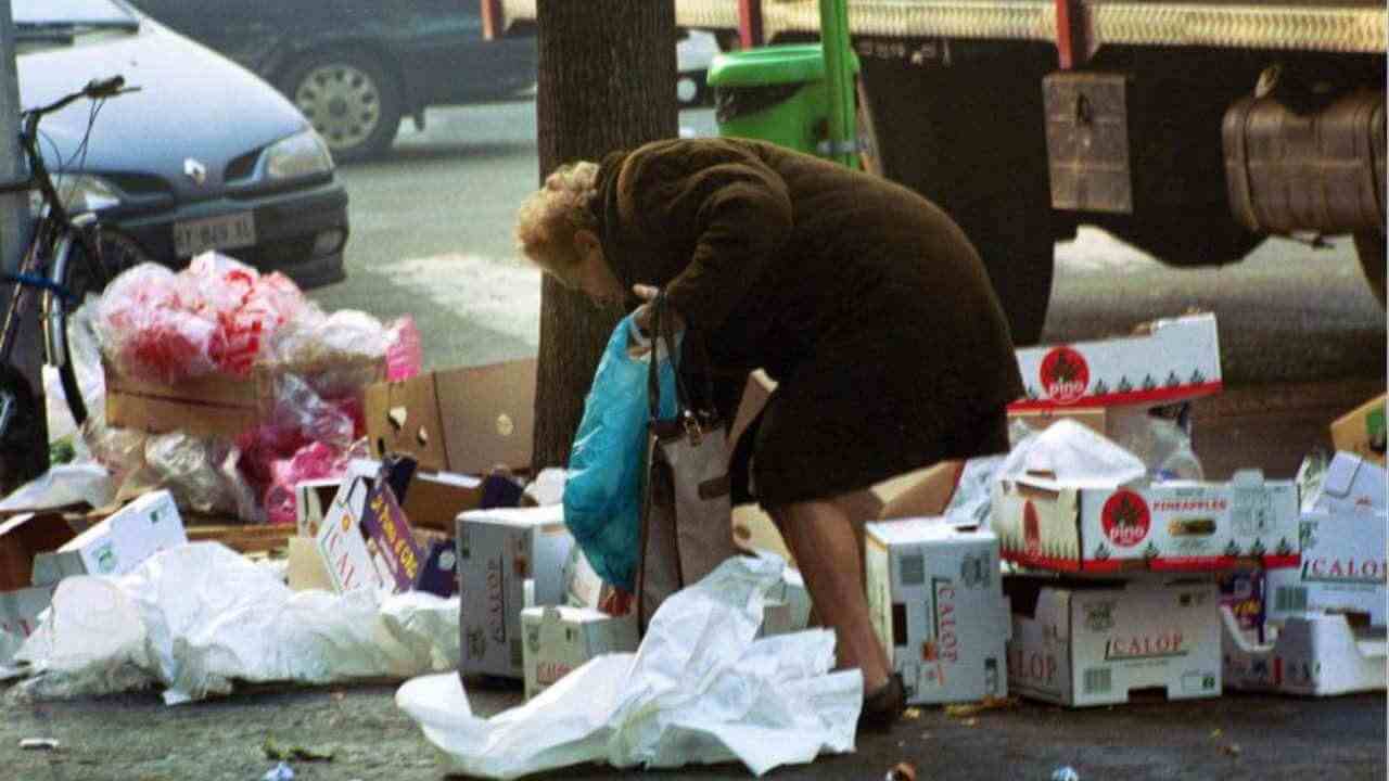 Una donna chinata che raccoglie tra i rifiuti qualcosa da mangiare, in segno della povertà