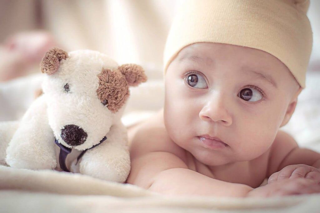 Un neonato disteso accanto a un peluche