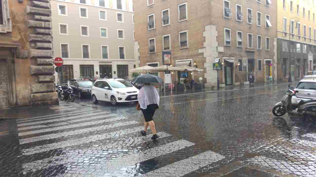 Maltempo, donna con ombrello attraversa una strada sulle strisce pedonali
