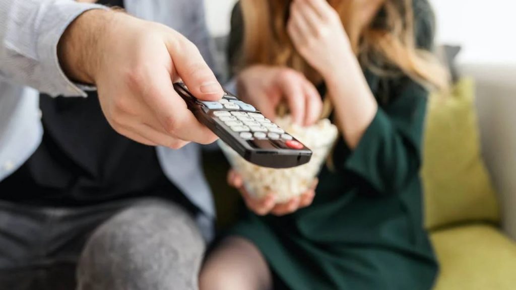 Un uomo e una donna che guardano la tv con un telecomando in  mano